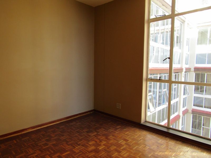An empty bedroom featuring original parquet flooring and a large window overlooking the building's internal courtyard.