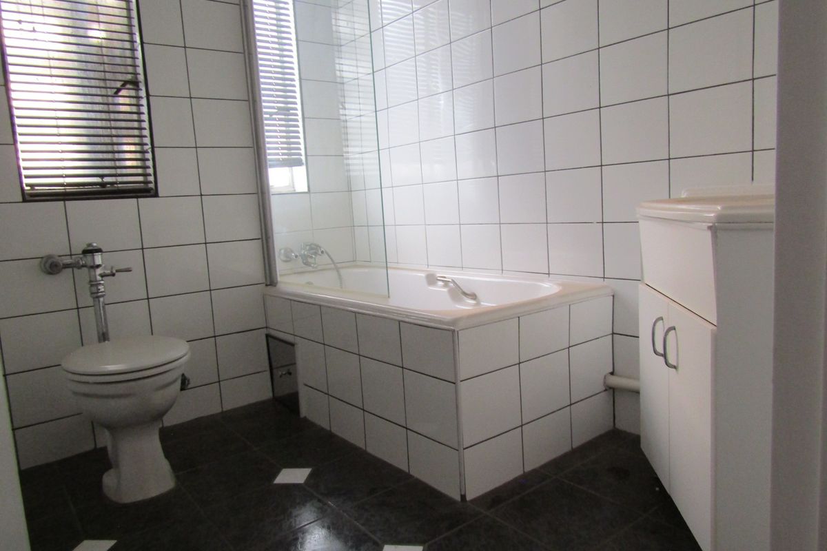 A functional bathroom featuring white wall tiles, a built-in bathtub with a glass screen, a toilet, and a vanity cabinet.