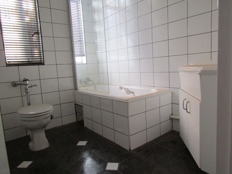 A functional bathroom featuring white wall tiles, a built-in bathtub with a glass screen, a toilet, and a vanity cabinet.
