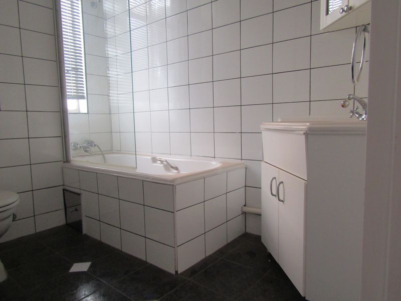 A functional bathroom featuring a tiled bathtub with a glass shower screen, a vanity unit with a basin, and a toilet.