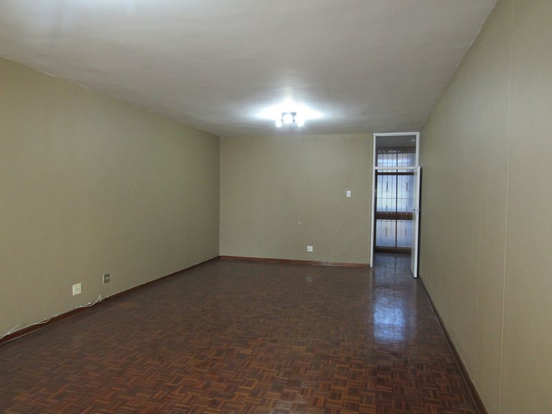 An empty living room featuring parquet flooring, neutral wall tones, and a security gate leading to an external area.