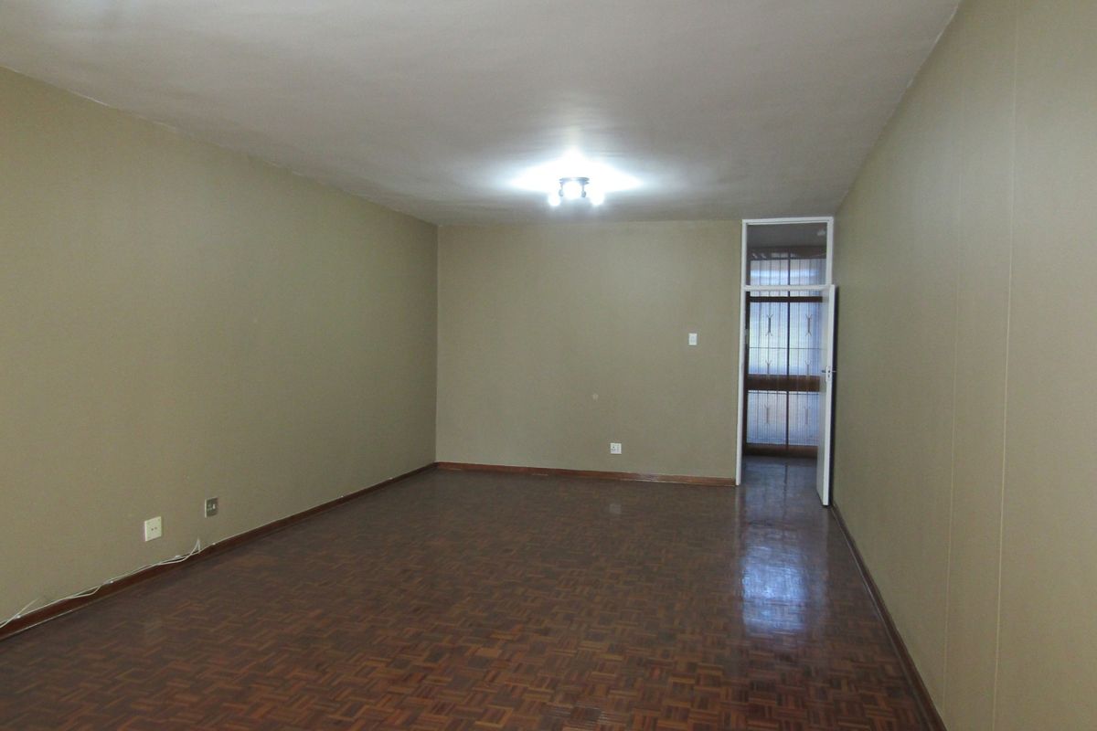 An empty living room featuring parquet flooring, neutral wall tones, and a security gate leading to an external area.