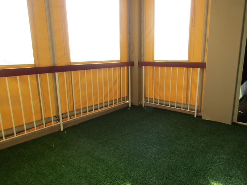 A covered balcony area featuring artificial grass flooring, a metal safety balustrade, and retractable yellow canvas privacy screens.