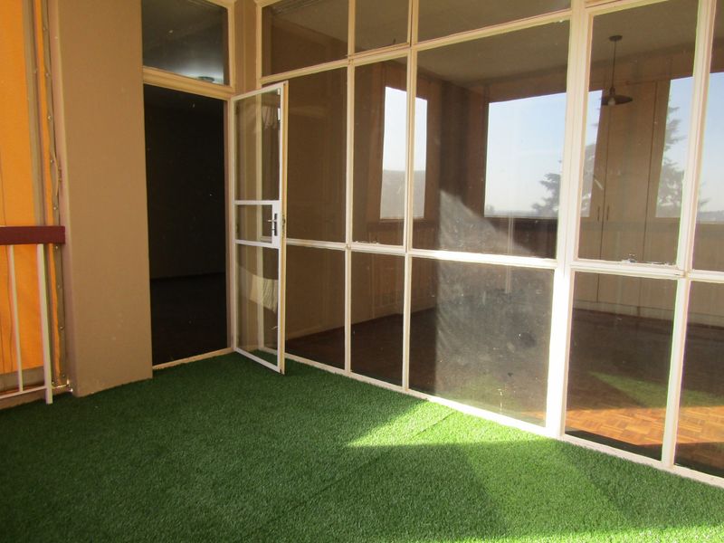 An enclosed balcony featuring artificial grass flooring and large glass panels, providing a bright and versatile outdoor living space.