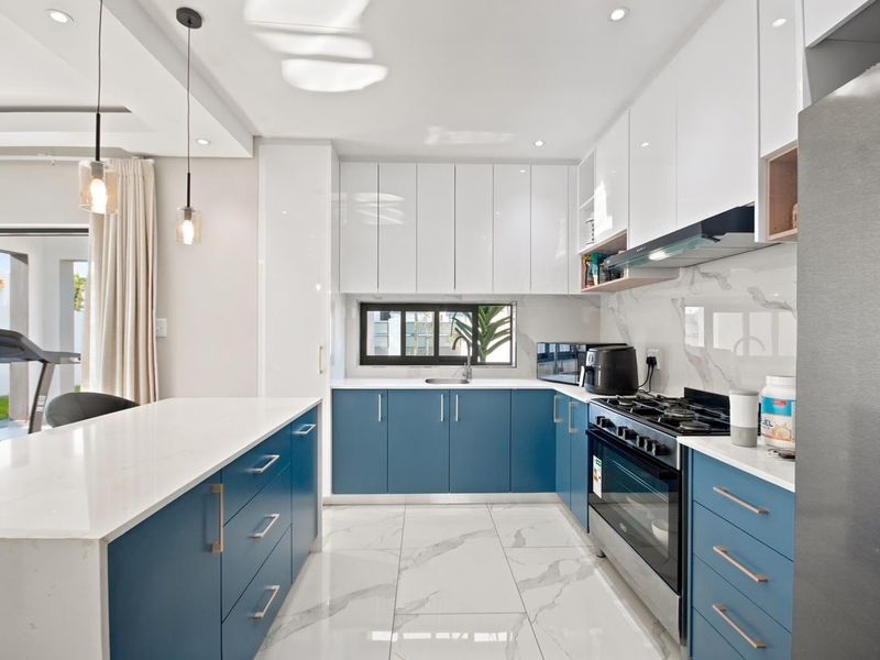 Modern kitchen featuring high-gloss blue and white cabinetry, quartz countertops, marble-look tile flooring, and integrated gas stove with extractor fan.