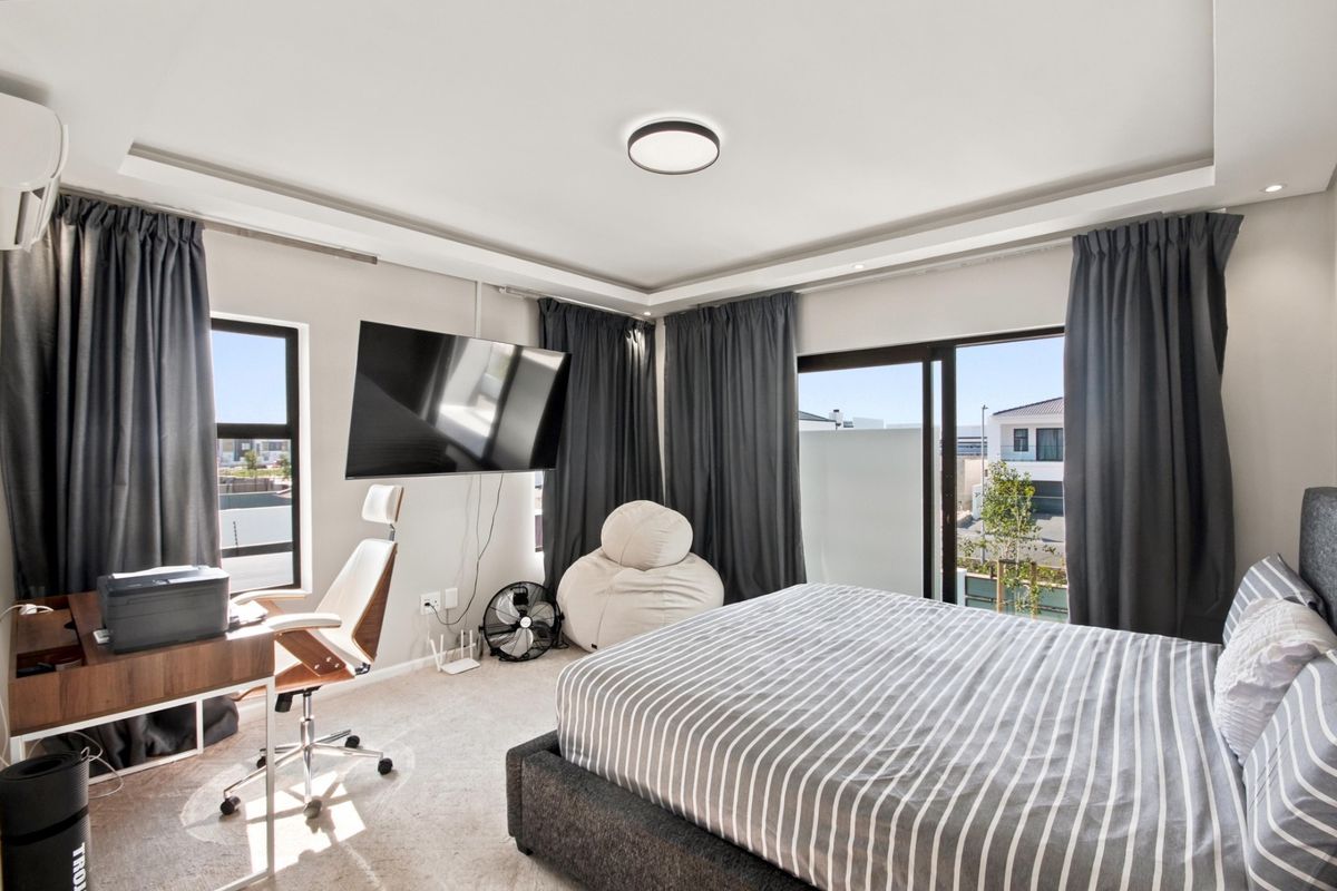 A well-lit bedroom featuring carpeted flooring, recessed ceiling lighting, a wall-mounted air conditioning unit, and a sliding glass door providing access to the exterior.