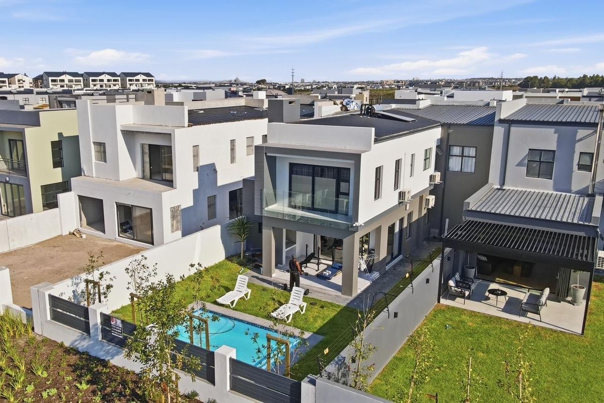 Aerial view of a modern two-story residential property featuring a private swimming pool, landscaped garden, and a covered patio area.