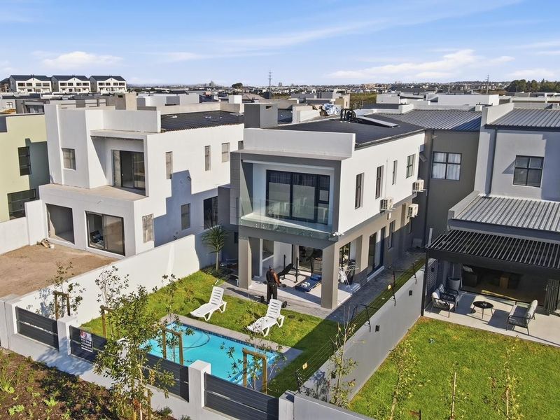Aerial view of a modern two-story residential property featuring a private swimming pool, landscaped garden, and a covered patio area.