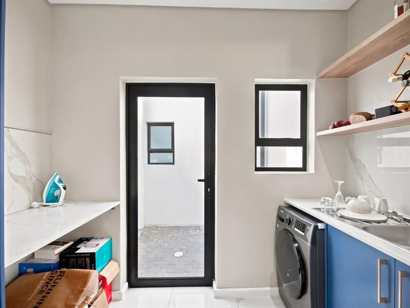 Modern laundry room featuring blue cabinetry, marble-look splashbacks, stainless steel sink, and floating timber shelving with direct access to an outdoor courtyard.