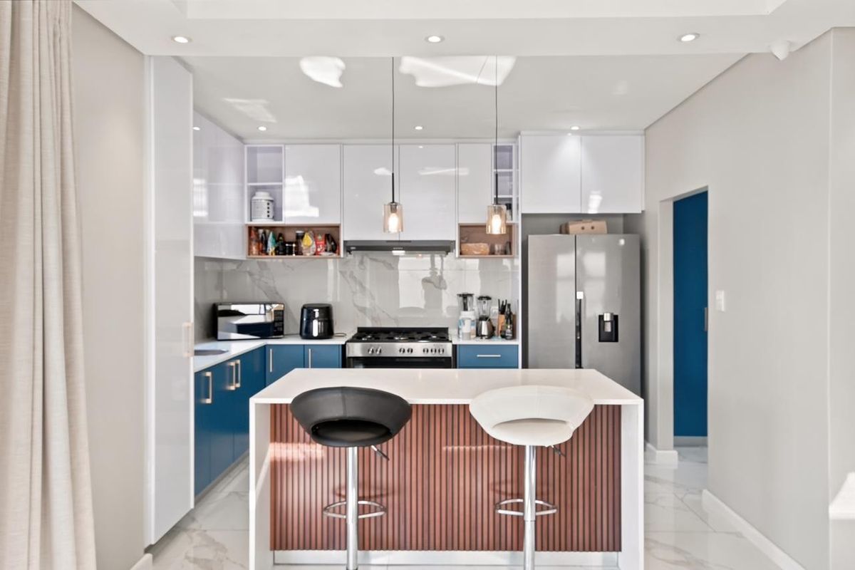 Modern kitchen featuring high-gloss blue and white cabinetry, a central island with wood-slat detailing, stone countertops, and integrated gas cooking appliances.