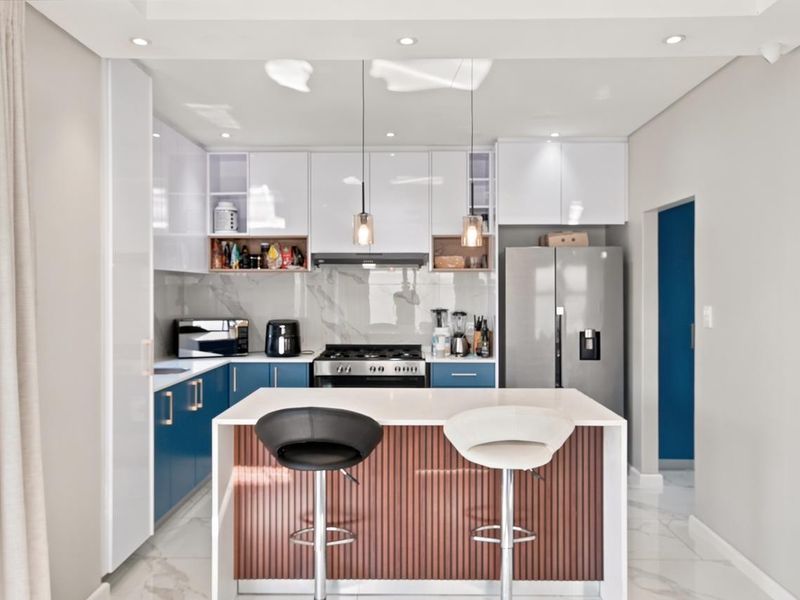 Modern kitchen featuring high-gloss blue and white cabinetry, a central island with wood-slat detailing, stone countertops, and integrated gas cooking appliances.