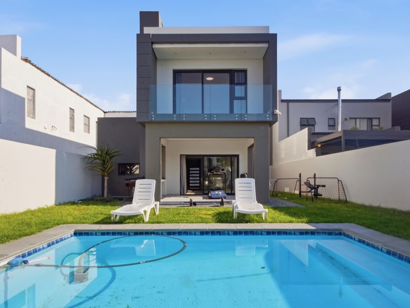 Rear view of a modern two-story house featuring a swimming pool, a ground-floor patio, and an upper-level balcony with glass balustrades.