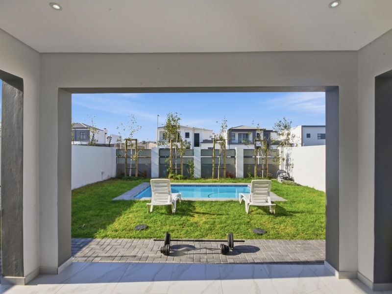 A covered patio area overlooking a private garden with a swimming pool and paved surround, offering a clean and modern outdoor living space.