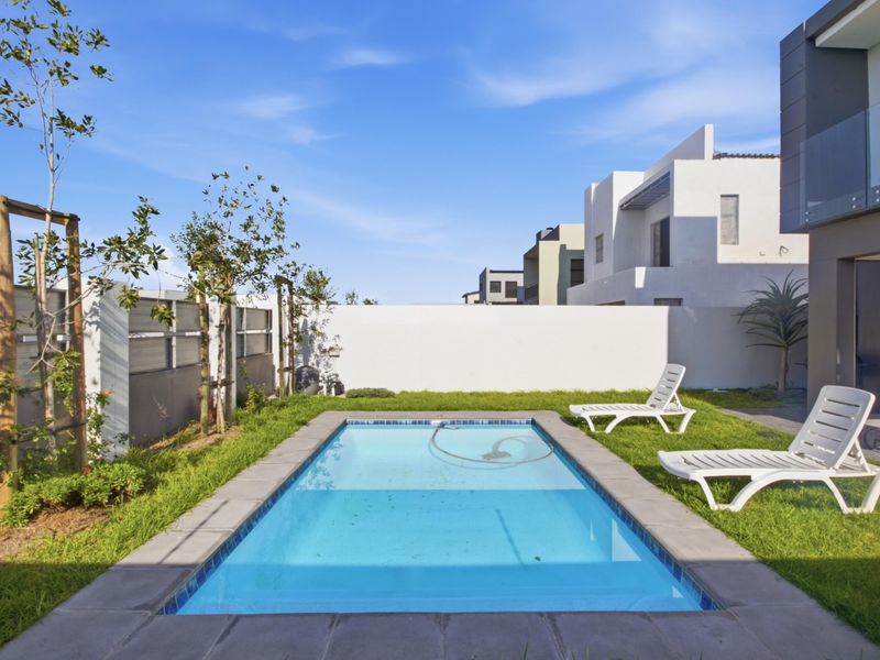 A private backyard featuring a rectangular swimming pool, paved surround, and a well-maintained lawn enclosed by a boundary wall.
