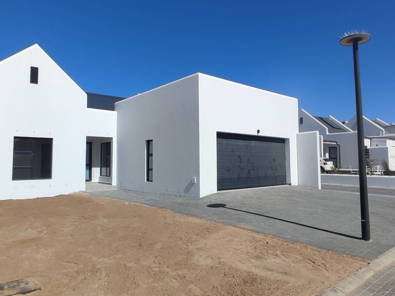 Modern contemporary house featuring a clean white facade, gabled roof design, and a paved driveway leading to a double garage.