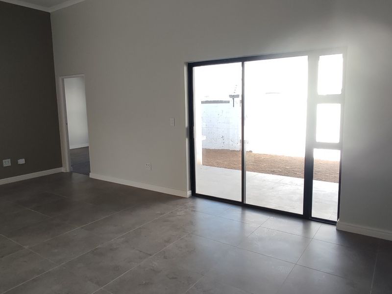 Modern open-plan living area featuring large format floor tiles, an accent wall, and a sliding door leading to the outdoor space.