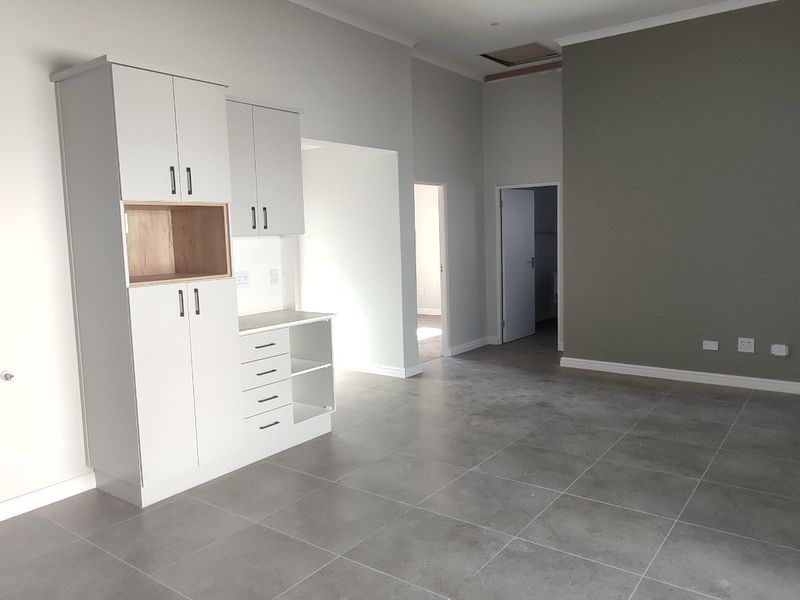 Spacious open-plan living area featuring modern grey tiled flooring, neutral wall tones, and built-in cabinetry, offering a clean and versatile layout.