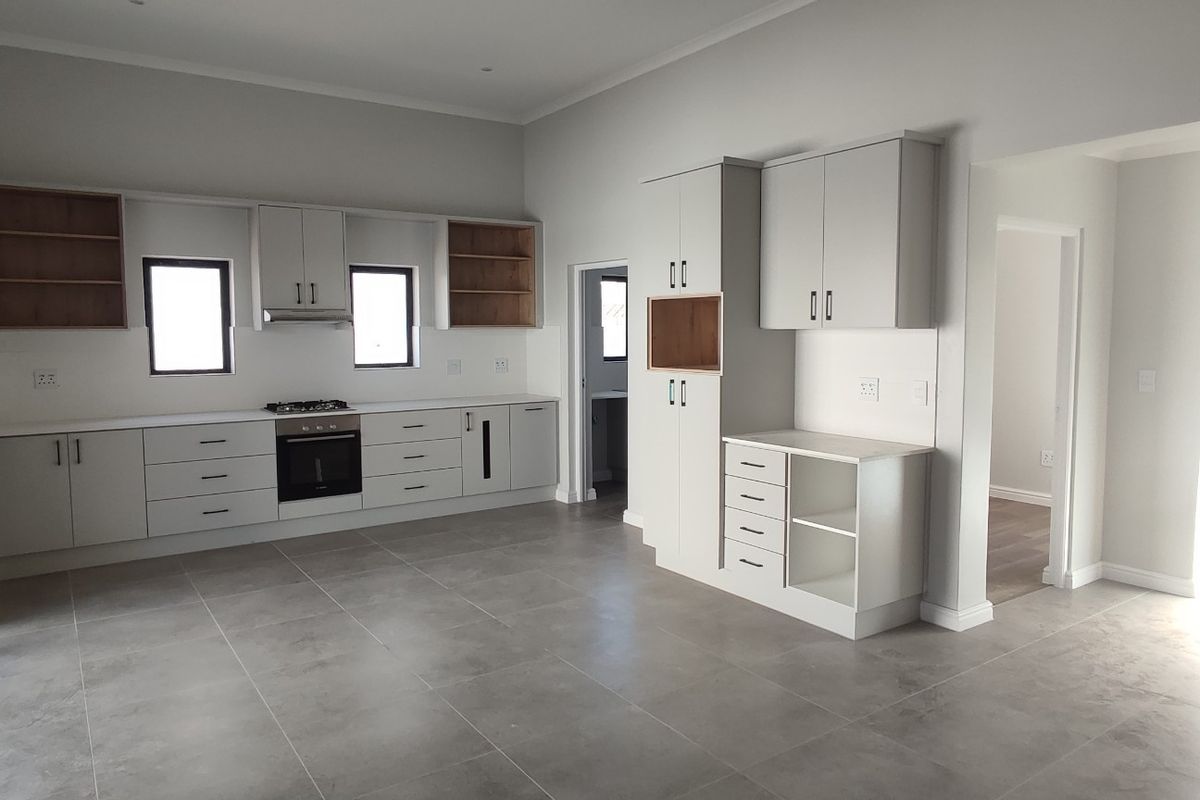 Modern, spacious kitchen featuring sleek built-in cabinetry, stone countertops, integrated oven and hob, and large format floor tiles in a neutral palette.