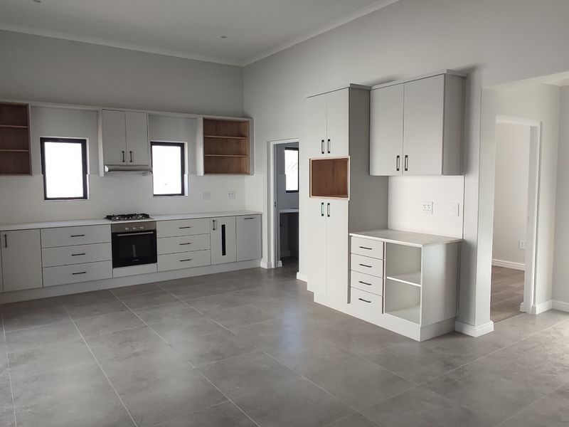 Modern, spacious kitchen featuring sleek built-in cabinetry, stone countertops, integrated oven and hob, and large format floor tiles in a neutral palette.