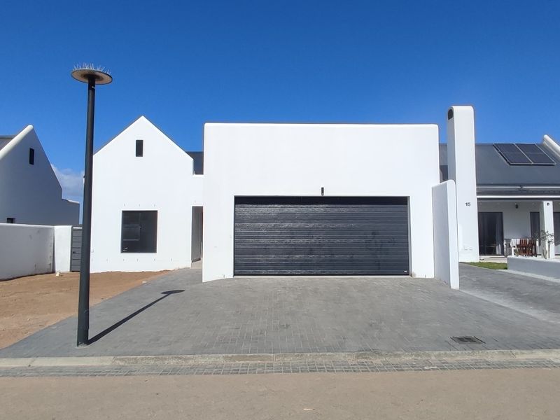 Modern white facade featuring a double garage, paved driveway, and solar panels, situated in a contemporary residential estate.