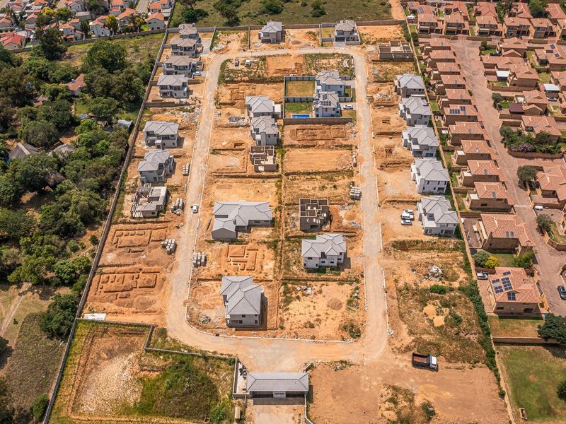 Aerial view of a residential housing development under construction, featuring multiple detached homes, paved internal roads, and a secure gated entrance.