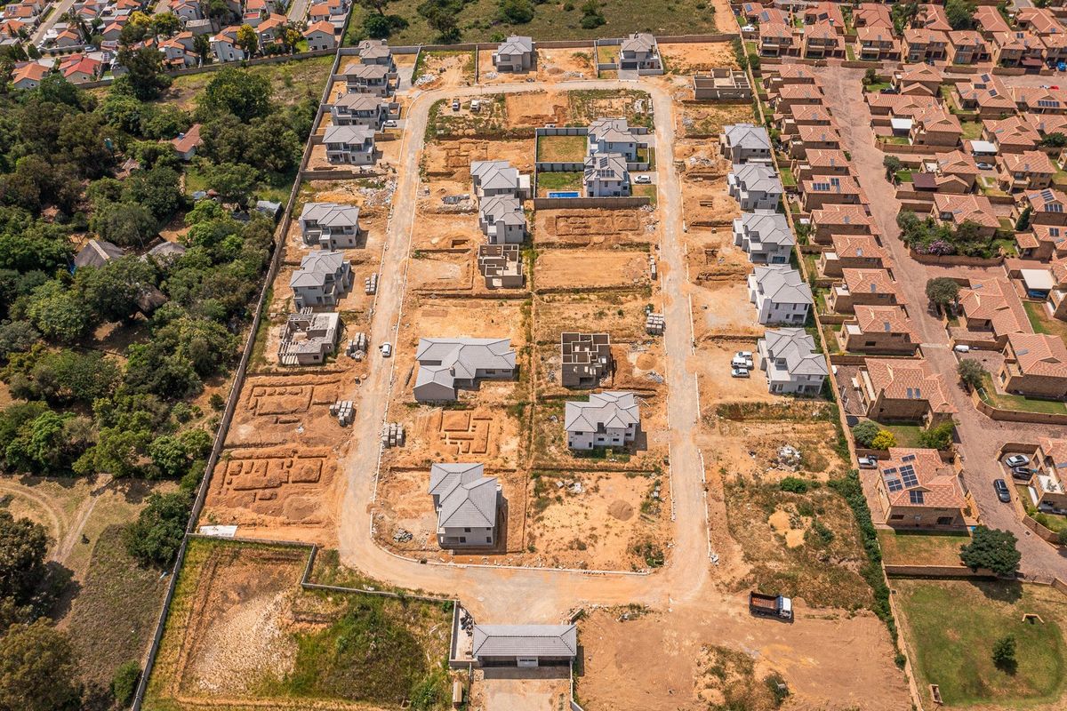 Aerial view of a residential housing development under construction, featuring multiple detached homes, paved internal roads, and a secure gated entrance.