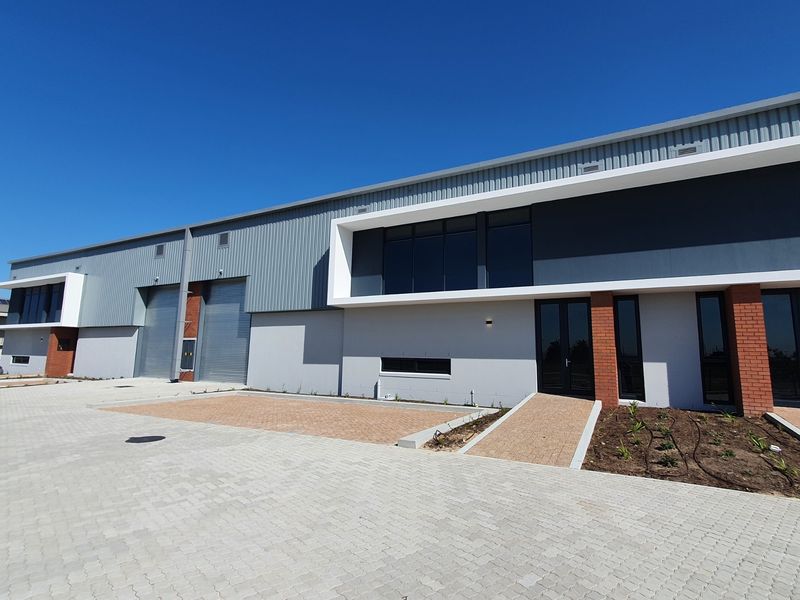 Modern industrial warehouse unit featuring roller shutter doors, paved exterior access, and contemporary metal and brick facade finishes.