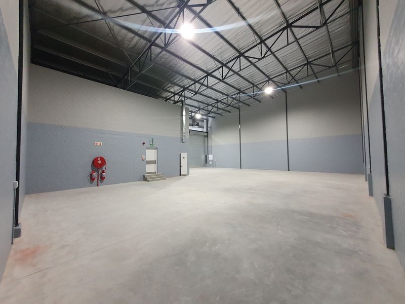 Spacious industrial warehouse unit featuring high ceilings with exposed steel trusses, polished concrete flooring, and integrated fire safety equipment.