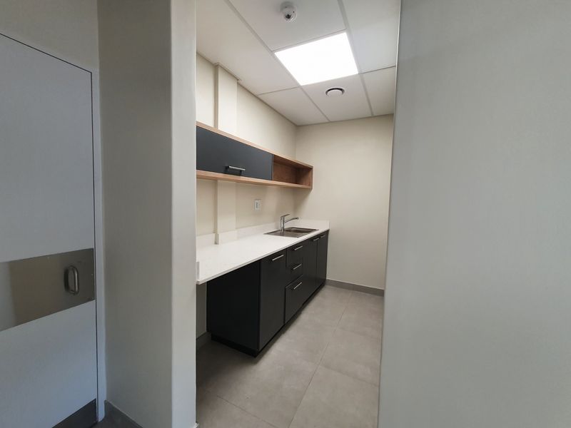 A clean, modern scullery or kitchenette area featuring dark cabinetry, stone countertops, a stainless steel sink, and professional recessed lighting.