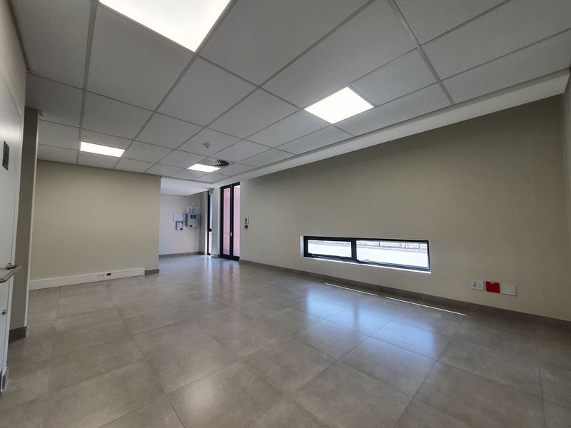 A modern, vacant industrial office space featuring neutral walls, large ceramic floor tiles, and a clean suspended ceiling with integrated LED lighting.