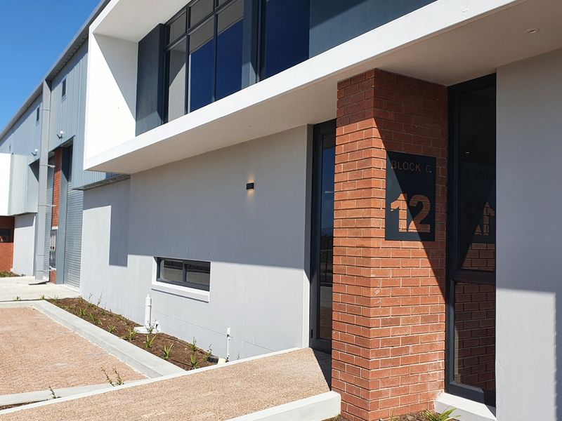 Modern industrial unit entrance featuring a combination of exposed brickwork, sleek metal cladding, and large aluminium-framed windows in a well-maintained business park setting.