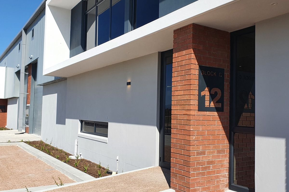Modern industrial unit entrance featuring a combination of exposed brickwork, sleek metal cladding, and large aluminium-framed windows in a well-maintained business park setting.