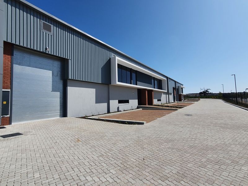 Modern industrial warehouse exterior featuring a large roller shutter door, corrugated metal cladding, and a spacious paved driveway area.