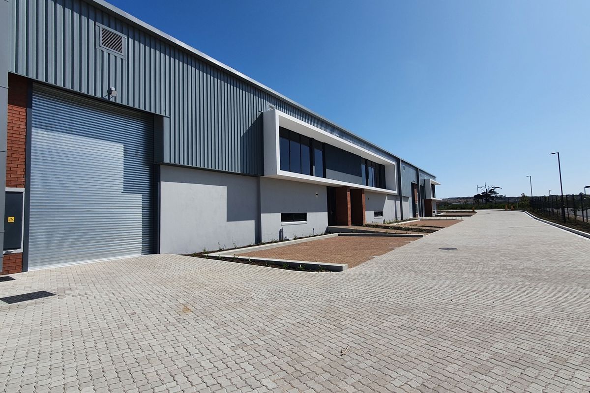 Modern industrial warehouse exterior featuring a large roller shutter door, corrugated metal cladding, and a spacious paved driveway area.