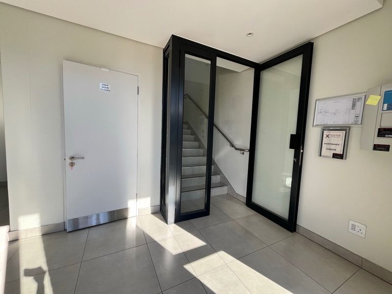 A clean, modern industrial hallway featuring tiled flooring, a glass-enclosed staircase, and minimalist white walls with professional finishes.