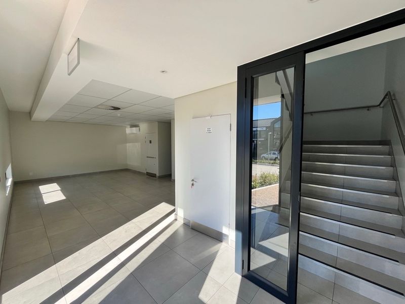 A bright, modern industrial entry foyer featuring tiled flooring, a suspended ceiling, and a glass-enclosed staircase leading to the upper level.
