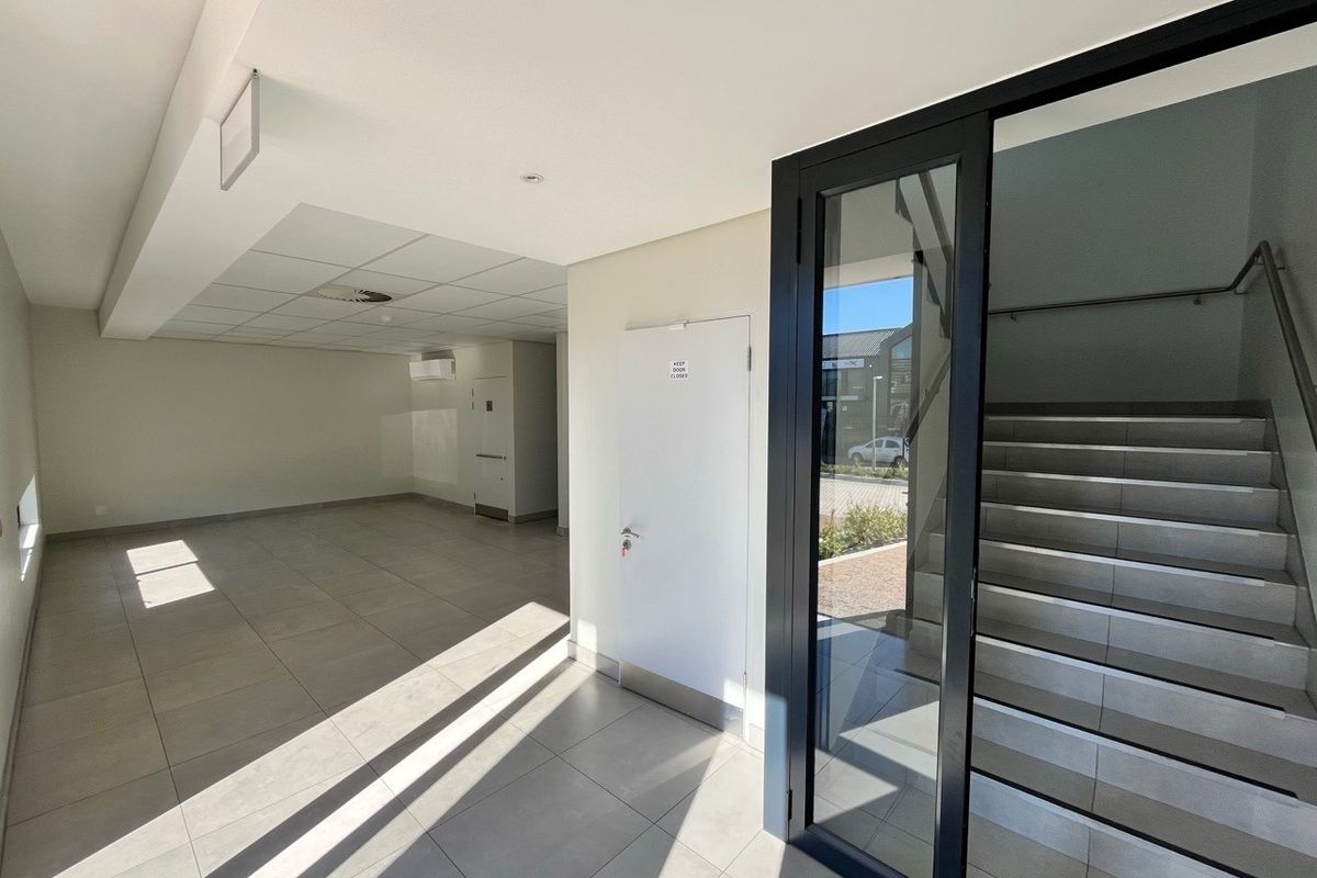 A bright, modern industrial entry foyer featuring tiled flooring, a suspended ceiling, and a glass-enclosed staircase leading to the upper level.