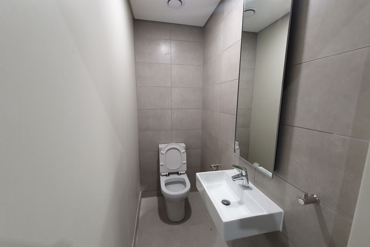 A modern, minimalist bathroom featuring a wall-mounted basin, toilet, and neutral grey wall tiles with a large mirror.