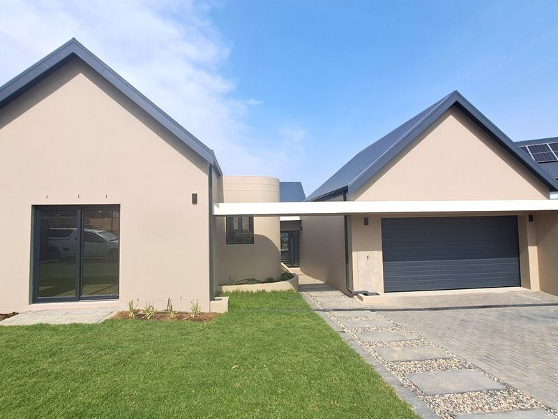 Modern single-story residence featuring a double garage, paved driveway, solar panels, and clean architectural lines with a well-maintained front lawn.