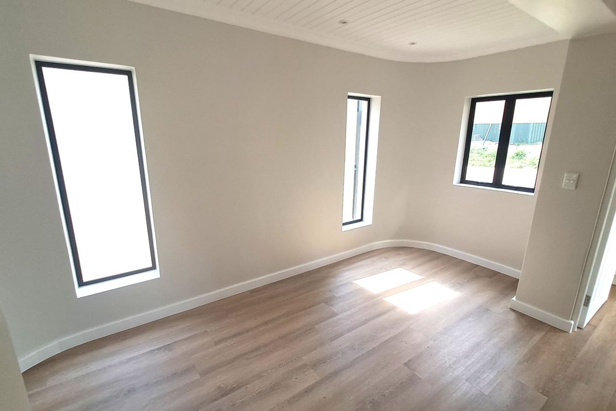 A bright, empty bedroom featuring modern laminate flooring, black-framed windows, and a stylish tongue and groove ceiling finish.