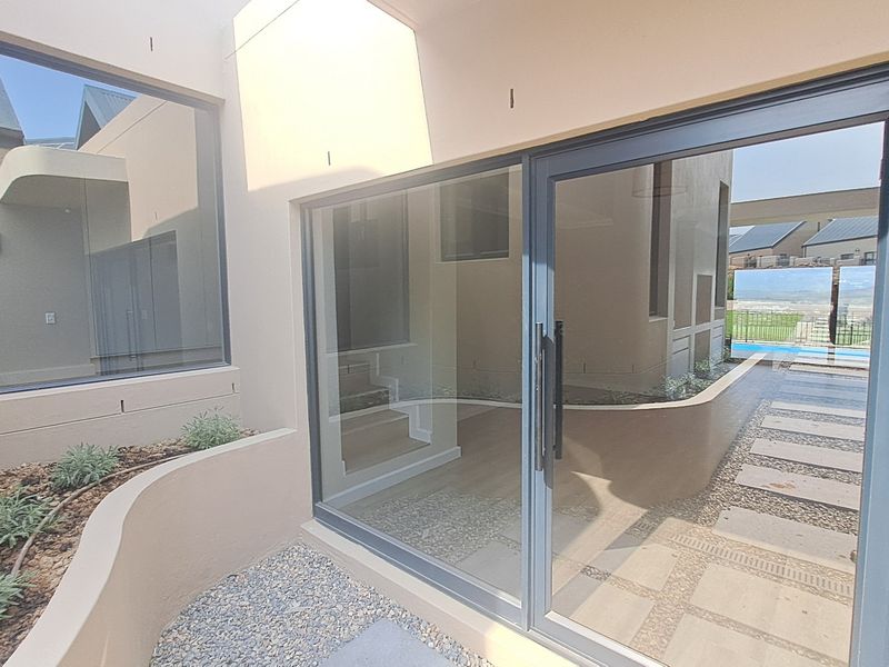 A modern, well-maintained outdoor patio area featuring large sliding glass doors, clean architectural lines, and a landscaped gravel garden bed.