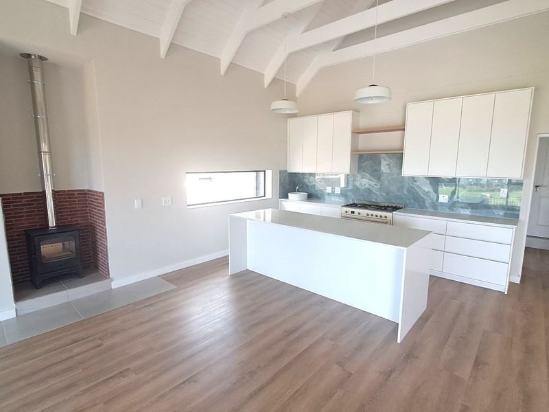 Spacious open-plan kitchen and living area featuring vaulted ceilings with exposed rafters, a modern kitchen island, and a built-in wood-burning fireplace.