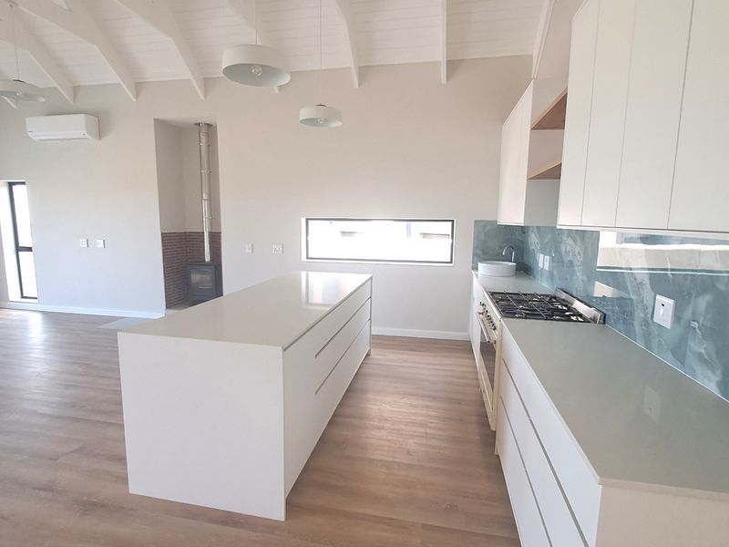 Spacious open-plan living area featuring a modern kitchen with stone benchtops, gas cooktop, and a cozy wood-burning fireplace under a vaulted ceiling.