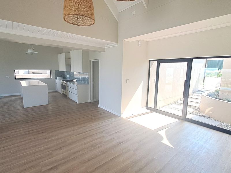 Spacious open-plan living area featuring a modern kitchen with island, vaulted ceilings, wood-burning fireplace, and large sliding doors opening to an outdoor space.