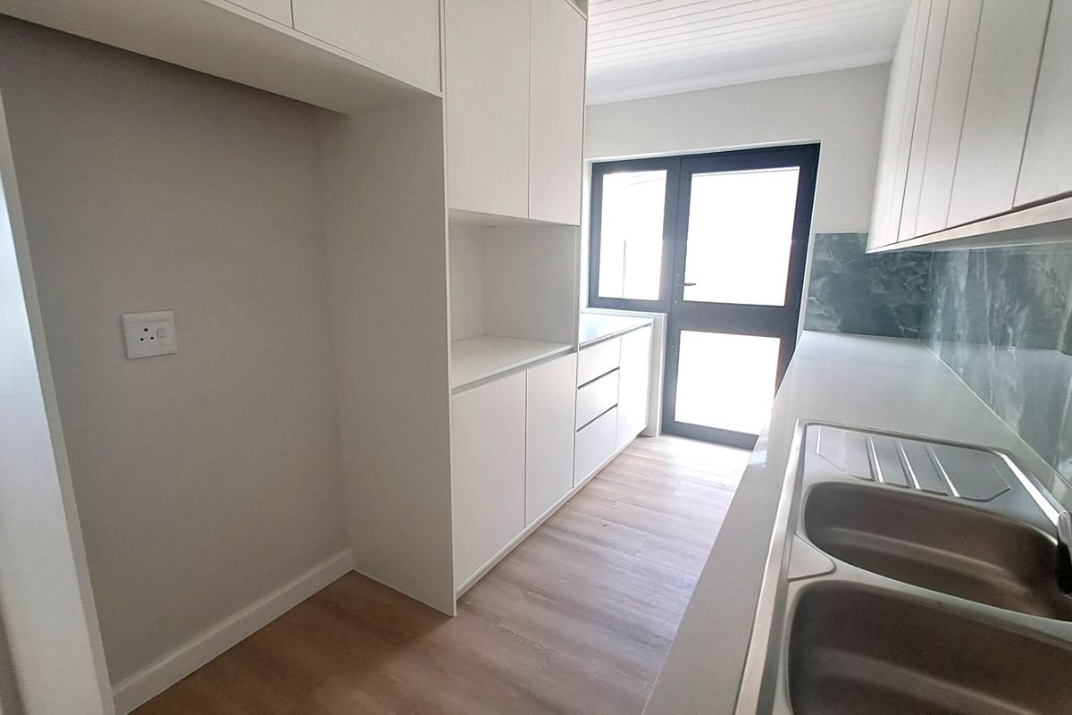 Modern kitchen featuring clean white cabinetry, stone countertops, a double bowl sink, and a stylish tiled splashback with direct access to the exterior.