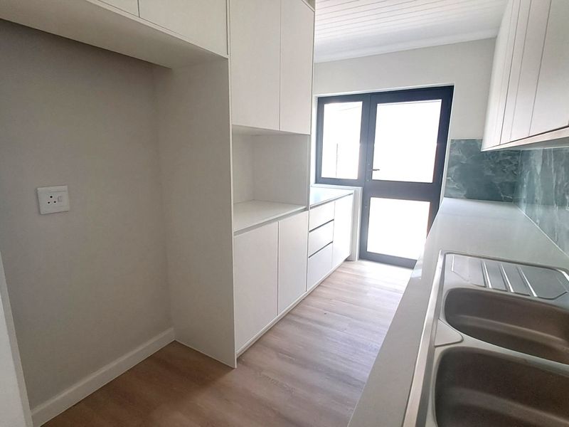 Modern kitchen featuring clean white cabinetry, stone countertops, a double bowl sink, and a stylish tiled splashback with direct access to the exterior.