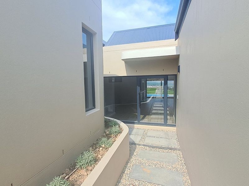 A modern exterior walkway featuring a paved path, raised planter box, and a large sliding glass door leading into the home.