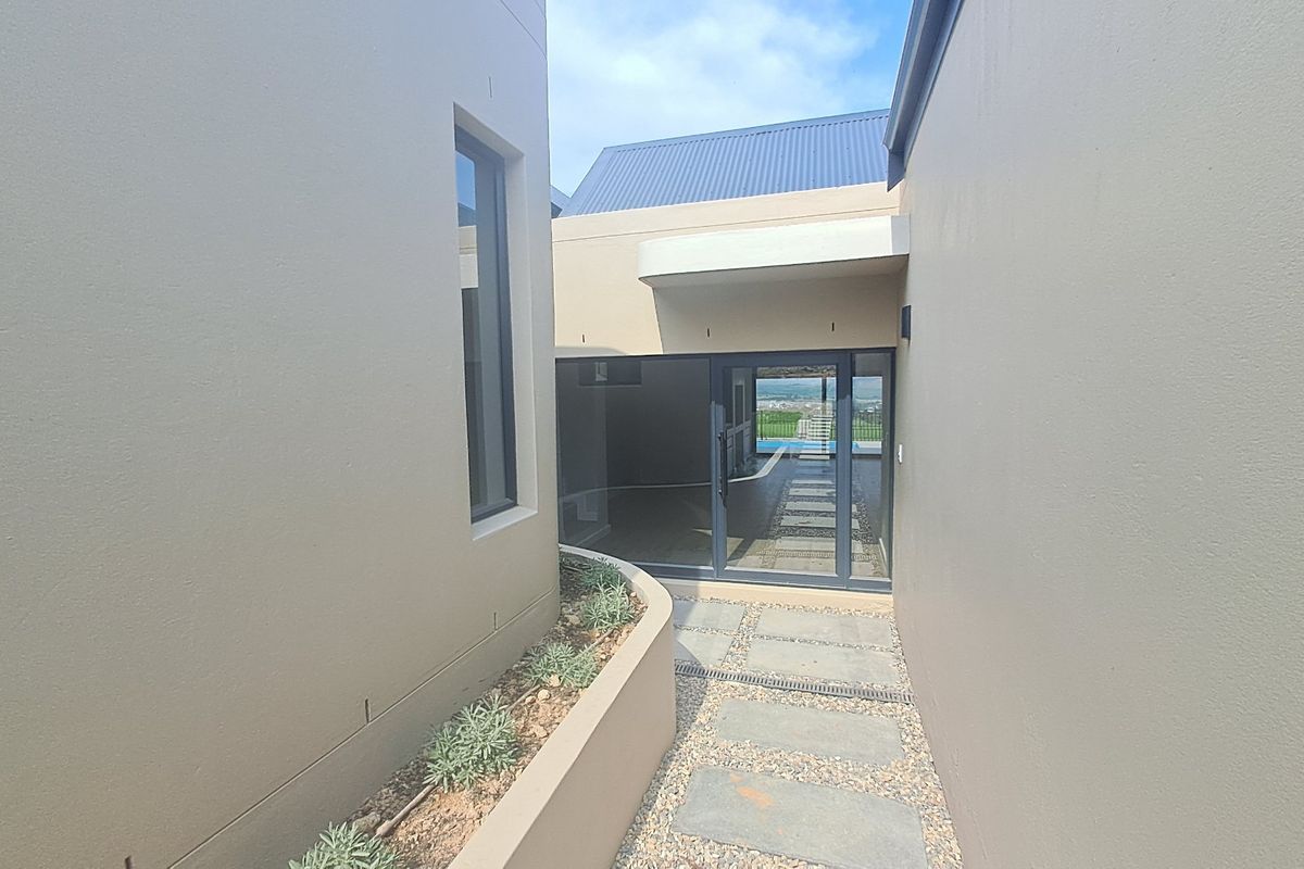 A modern exterior walkway featuring a paved path, raised planter box, and a large sliding glass door leading into the home.