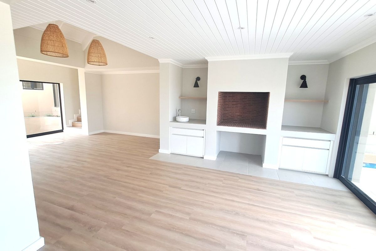 Spacious open-plan living area featuring a built-in braai, custom cabinetry with a prep sink, vaulted tongue and groove ceilings, and modern laminate flooring.