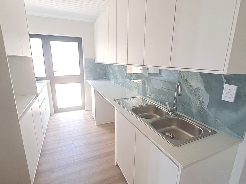 Modern scullery featuring clean white cabinetry, a double stainless steel sink, and a stylish stone-look splashback with direct access to the exterior.